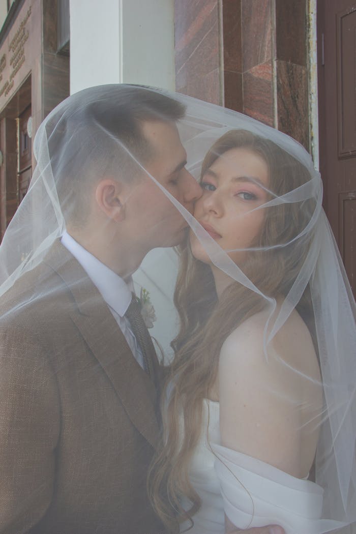 Bride and groom share a tender kiss under a veil, capturing a romantic wedding moment.