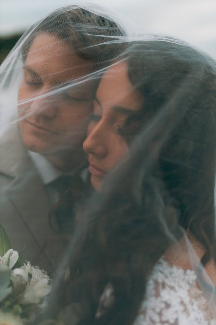 A tender moment between a wedding couple under a delicate veil, capturing love and intimacy.